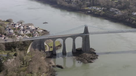 aerial view of menai suspension bridge, flying right to left around the bridge while zooming out, anglesey, north wales, uk