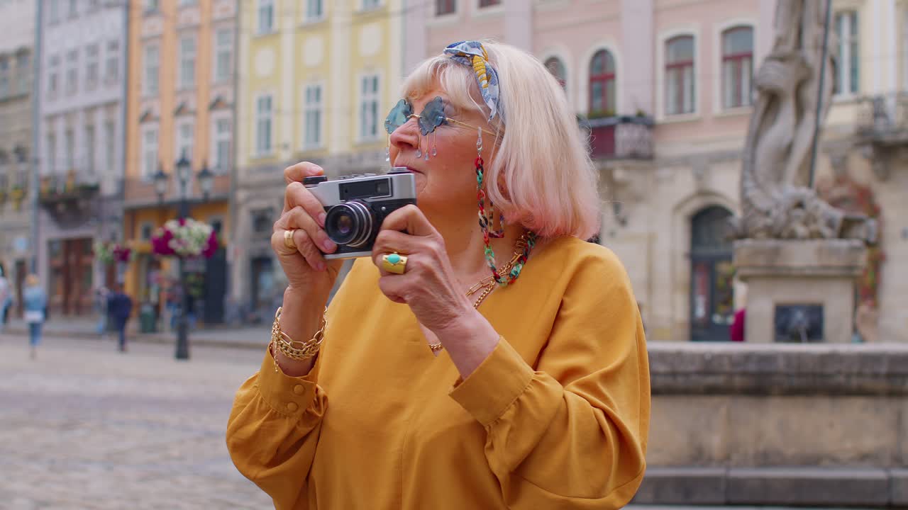 Anziana turista che scatta foto con la macchina fotografica nel centro città in estate, vita dopo il pensionamento