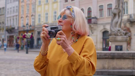 senior woman tourist taking pictures with photo camera in summer city center, life after retirement