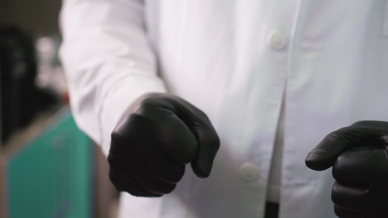 A close-up view of a man wearing black gloves clamping his hands together continuously, with a blur view of shelf behind and somethings in the shelf