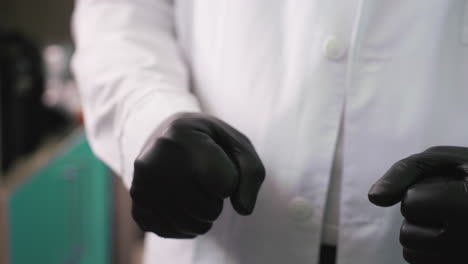 a close-up view of a man wearing black gloves clamping his hands together continuously, with a blur view of shelf behind and somethings in the shelf