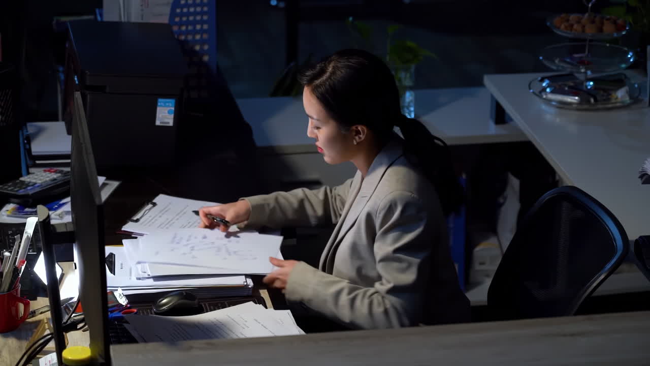 Young office worker is working late into the night at her desk in office, she grapples with stress and anxiety as deadlines loom and exhaustion sets in