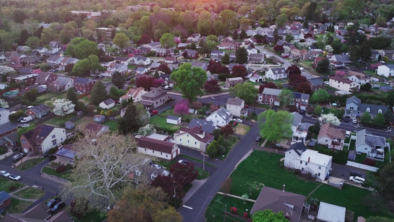 Vista aérea de drone ao pôr do sol de um exuberante bairro suburbano da Filadélfia com casas unifamiliares, árvores floridas de primavera, jardins e flores coloridas na hora dourada.