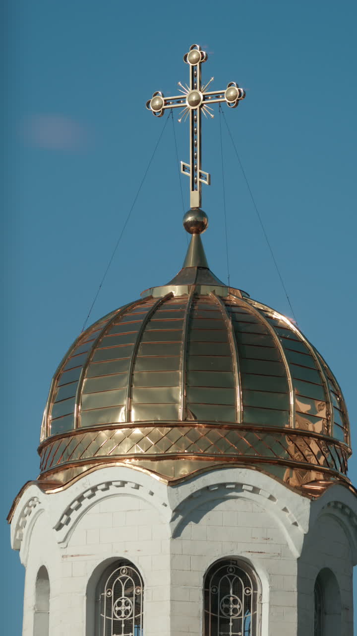 Elegant metallic church cross glowing under clear blue sky. Vertical