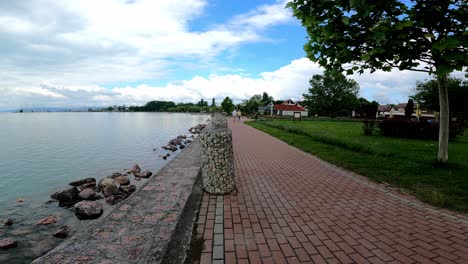 People-Walking-On-Promenade-By-The-Lake-Balaton-In-Balatonfuzfo,-Hungary