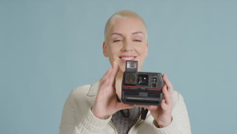 female caucasian model posing with instant film camera against blue backdrop 02