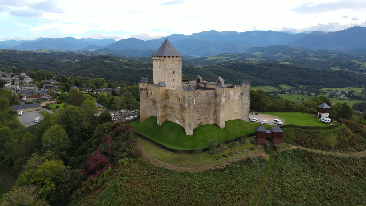 una toma aérea del castillo de mauvezin en la cima de una colina verde.