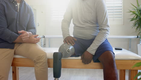 man with prosthetic leg sitting on table, discussing with therapist in clinic