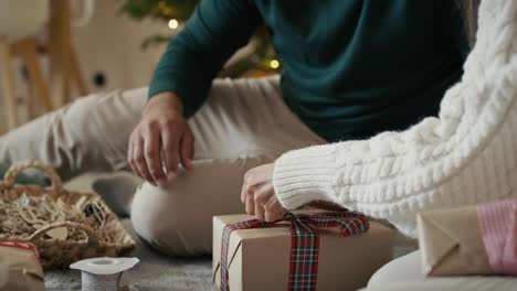 Hands-of-unrecognizable-couple-packing-Christmas-present-together-at-home.