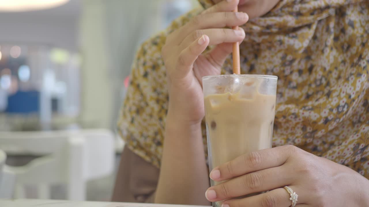 Close-up of a person holding a glass of iced coffee with a straw
