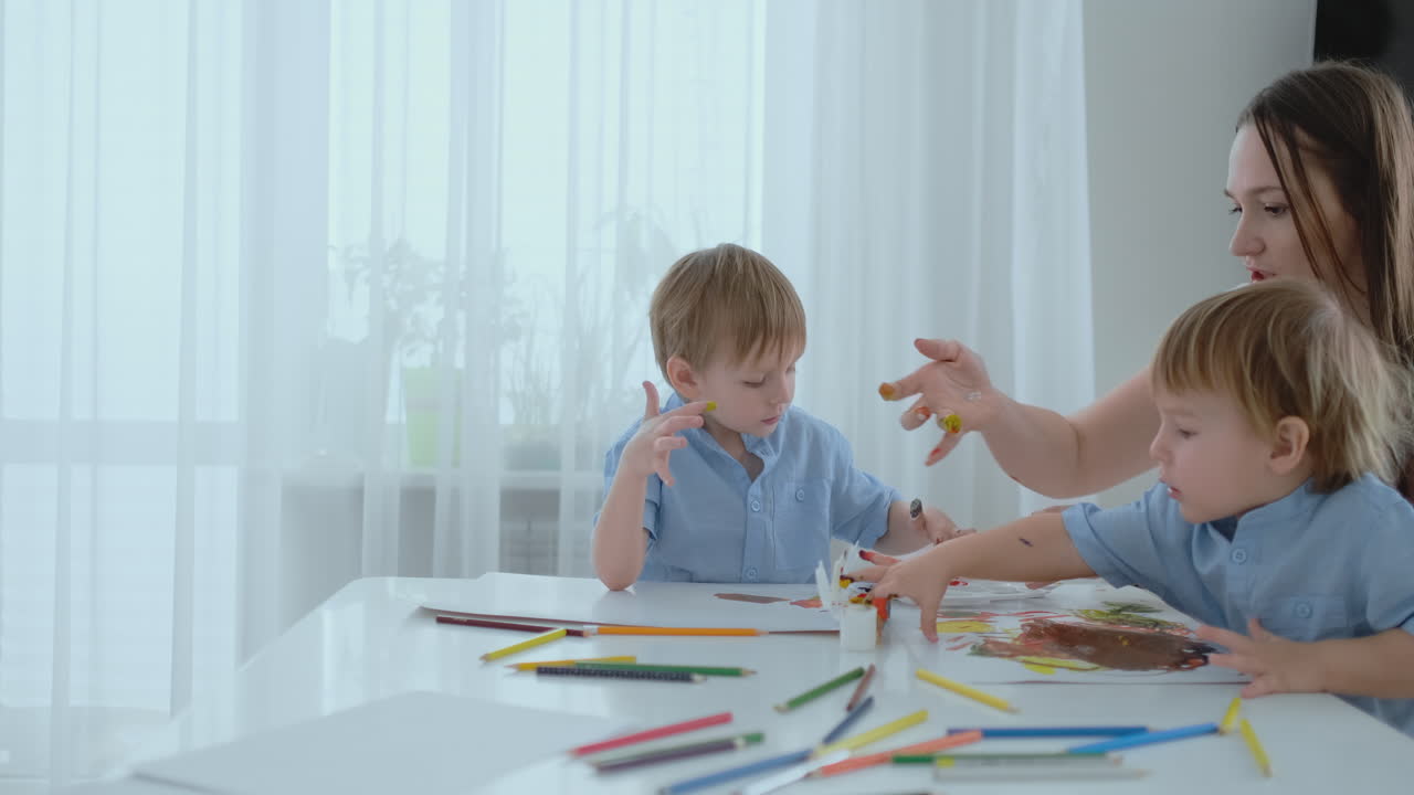 Two children of boys and mother are engaged in creative development doing homework by fingering on paper. The development of tactile sensations and small mathematics.