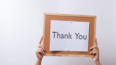 woman's hand shows the paper on board with the word thank you in white studio background with copy space