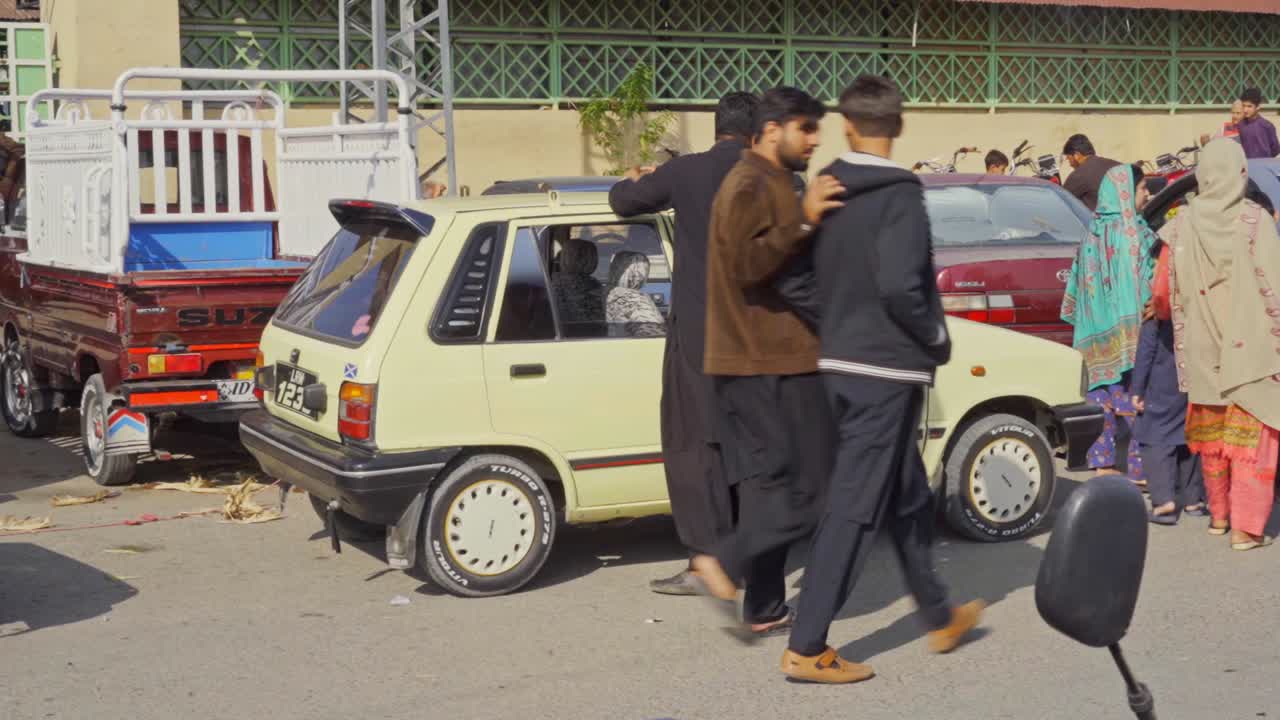 Islamabad taxi driver waits calmly for customers outside a vibrant market teeming with shoppers vendors and local activity in Pakistan