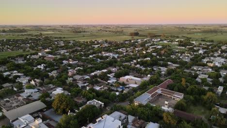 Dolly-Volando-Sobre-La-Soñadora-Ciudad-Verde-De-Santa-Elisa-Con-Tierras-De-Cultivo-Al-Fondo-Al-Atardecer,-Entre-Rios,-Argentina