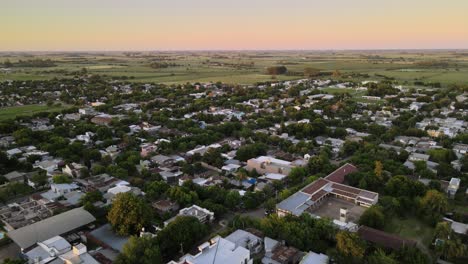 dolly in flying over dreamy santa elisa green countryside town with farmlands in background at sunset, entre rios, argentina