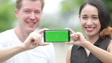 joven pareja multiétnica mostrando el teléfono juntos en las calles al aire libre