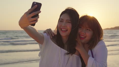 young asian lesbian couple using smartphone taking selfie near beach. beautiful women lgbt couple happy relax enjoy love moment when sunset in evening. lifestyle lesbian couple travel on beach concept