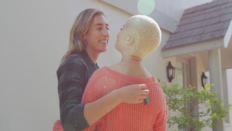 una feliz pareja de mujeres diversas abrazándose y sosteniendo las llaves al lado de la casa