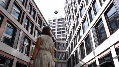 Young-attractive-business-woman-looks-around-turning-between-tall-office-buildings-in-financial-district