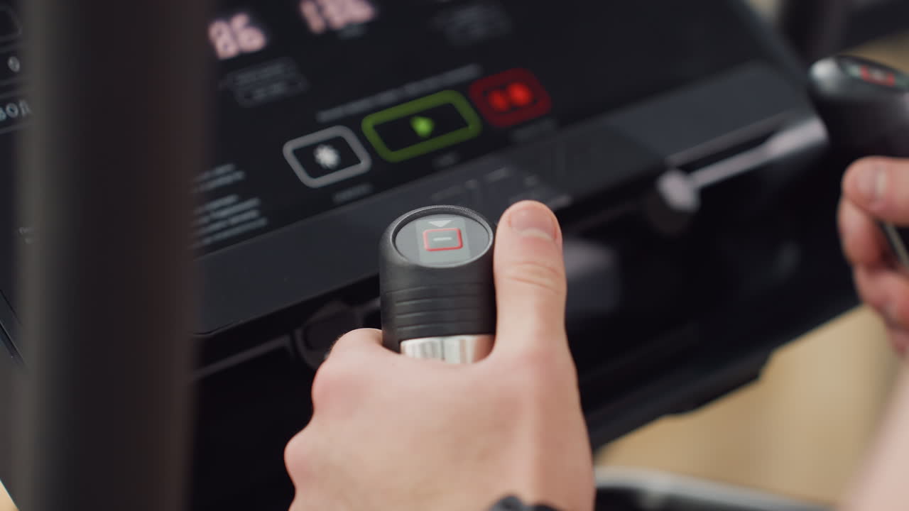 Console view of modern elliptical machine showing illuminated screen with heart rate and handle reflection as gym goer adjusts settings for cardio workout intensity under natural light