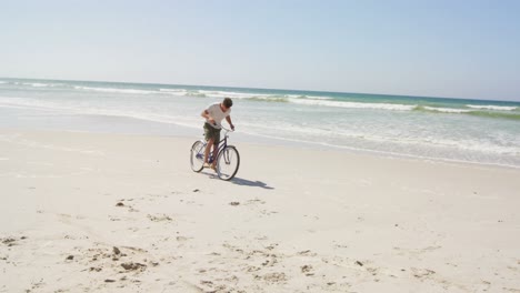 Man-riding-a-bicycle-at-beach-on-a-sunny-day-4k