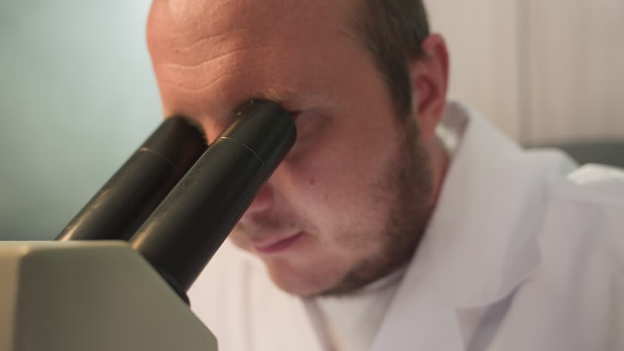 기술자가 실험실에서 현미경에 눈을 맞추는 근접한 모습, 전면은 현미경 렌즈를 보여줍니다.