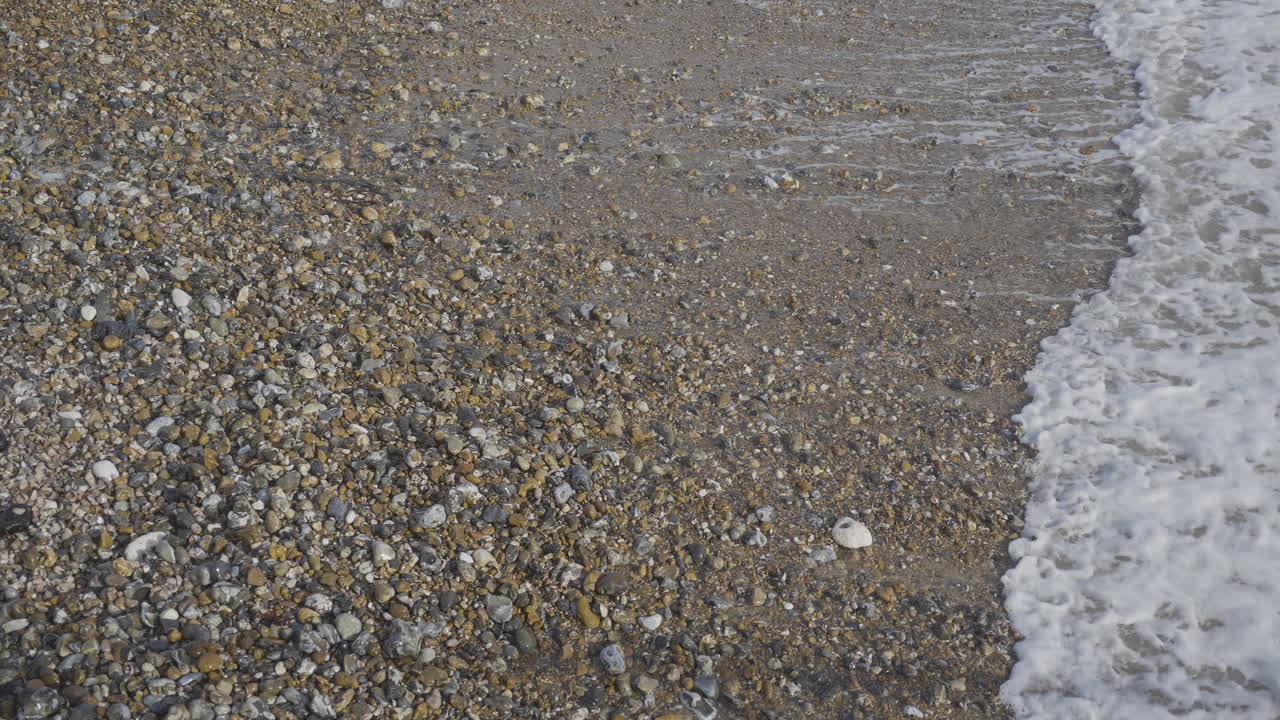 Ondas entrando e saindo em praia de pedras em câmera lenta