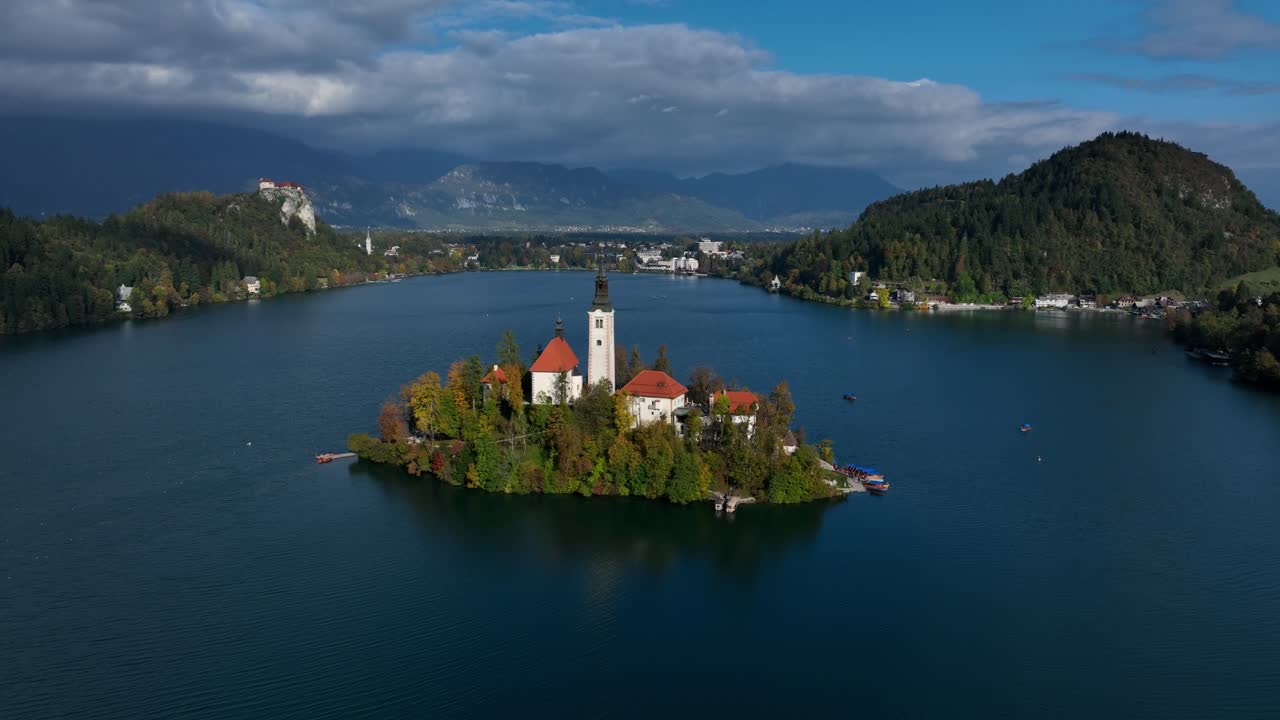 Urokliwa Wyspa Bled na Jeziorze Bled – ujęcie z drona oddalające się w słoneczny dzień.
