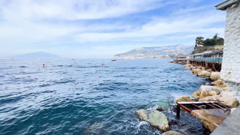 serene coastal view of the mediterranean sea from a rocky shore with a wooden pier in the foreground and mountains in the distance - sorrento, italy