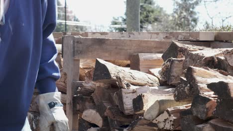 Hombre-Con-Camisa-Azul-Y-Guantes-De-Trabajo-Apila-Leña-En-Una-Pila-Ordenada