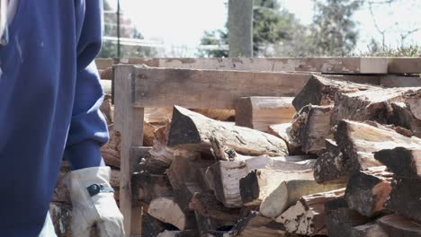 man in blue shirt and work gloves stacks fire wood into a neat pile