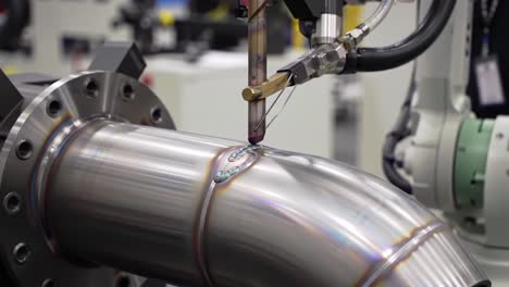 precision welding process in a controlled environment: close-up visuals of robotic arm and metallic tube interface showcasing advanced manufacturing techniques