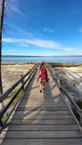 vertical view, following young woman with backpack walking on trail in yellowstone national park usa