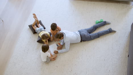 top view of sibling kids and dad sitting and lying on warm floor