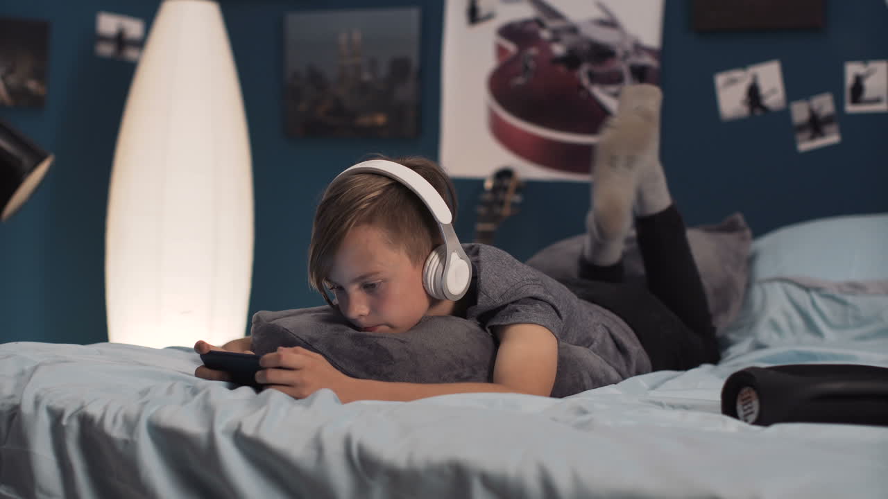 Boy Relaxing in Bedroom with Headphones and Phone