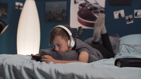 boy relaxing in bedroom with headphones and phone