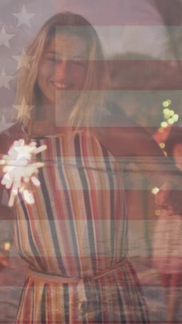 animation of flag of united states of america over happy diverse friends with sparklers on beach