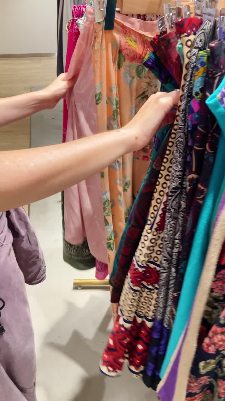Close up on female hands searching and browsing thrifting through second hand clothes in vintage fashion store. Buying cheap boutique sustainable wear. Gen Z hipster boho woman looking for used items