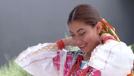 film clip of a young brunette latina dressed in the traditional costume called cayambeñas putting on her red necklace and smiling