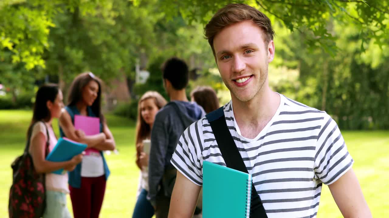 estudiante sonriente posando y compañeros de clase hablando detrás de él