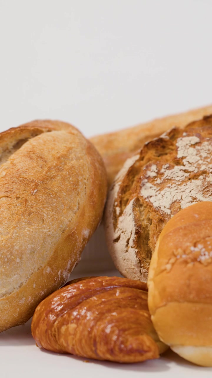 Primo piano di mani che afferrano pagnotte di pane artigianale e croissant su sfondo bianco.