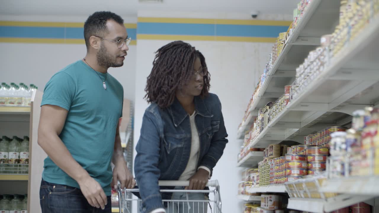 una pareja de jóvenes sonrientes de pie cerca de los estantes con productos enlatados