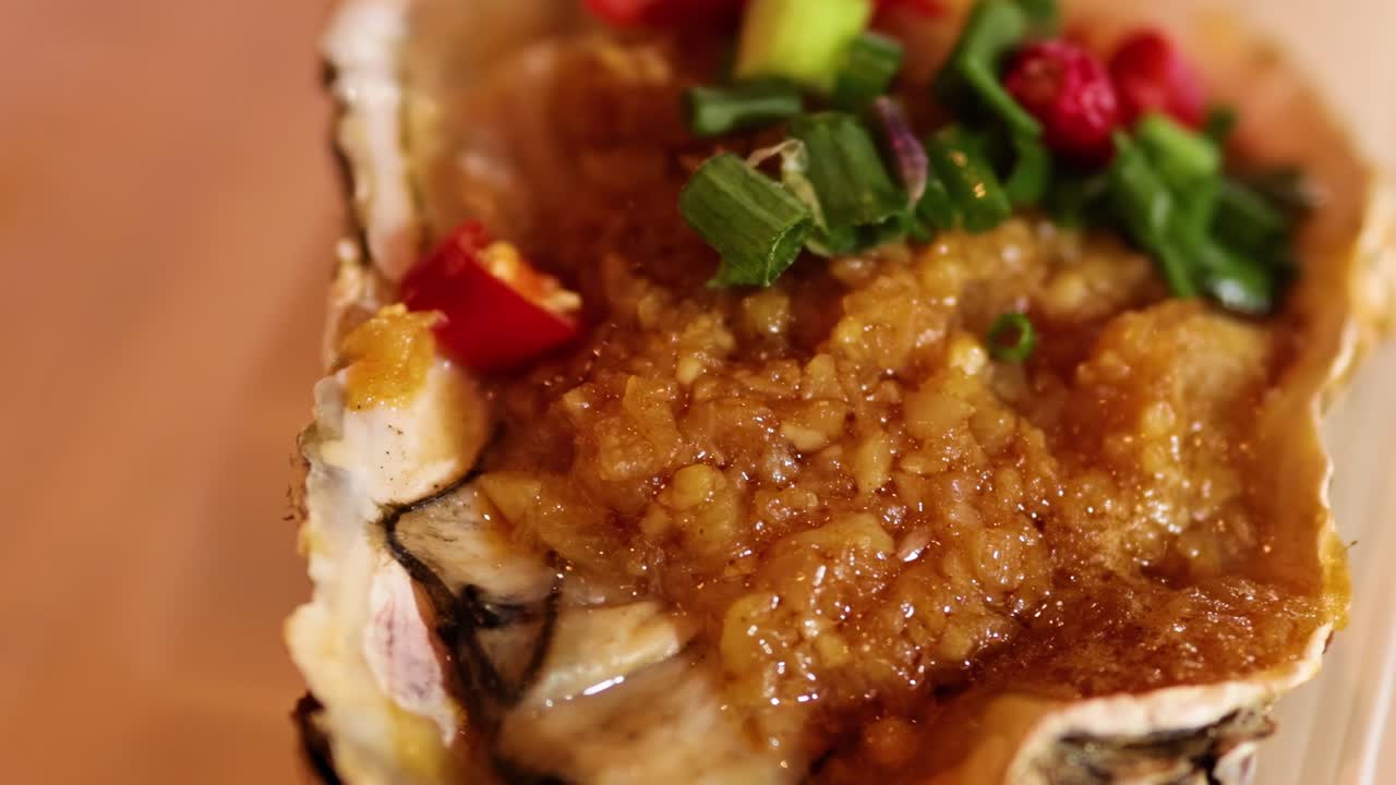 A detailed view of an oyster topped with garlic sauce, green onions, and red chili slices.