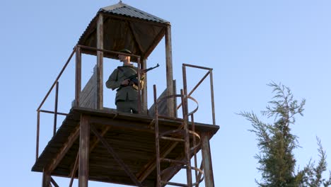 an armed army guard stands on lookout, high in a watch tower