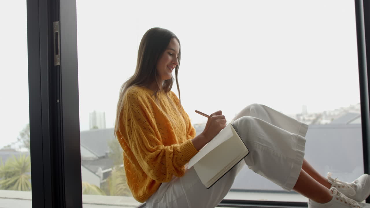 Writing in journal, woman sitting by window in cozy home setting, copy space