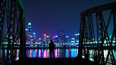 silhouette of people on a bridge at night, looking at a city skyline reflected in the water.