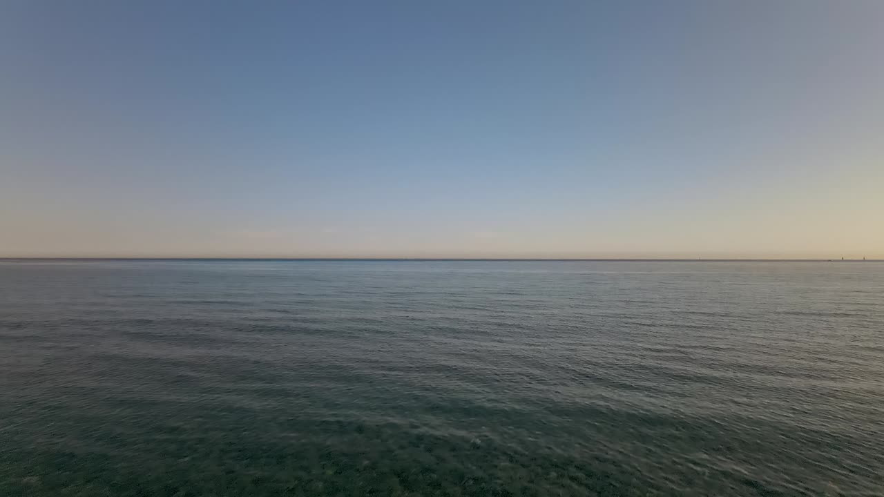 Aerial forward dolly shot of beach with man in the middle, from the sand into the ocean