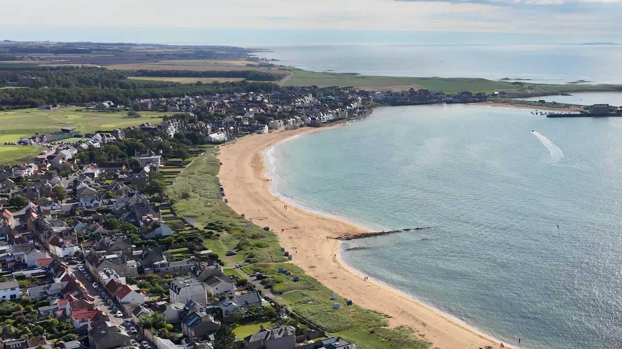 Drone pans above seaside town, sandy beach, and golf course under bright daylight, Fife, Scotland