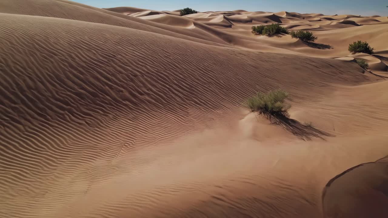 Aerial video captures sweeping desert dunes under a clear sky, showcasing the vast