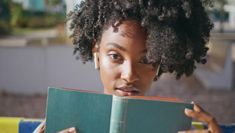 retrato de un estudiante posando sosteniendo un libro cerca de la cara en la calle sunny.
